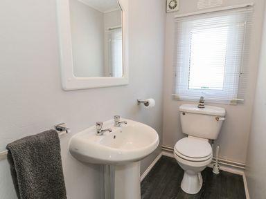 A bathroom with a pedestal sink mirror towel holder toilet with a window behind at Orchard Lodge Llanengan near Abersoch