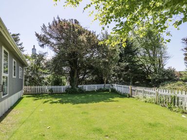 A backyard with green grass trees and a white picket fence at Orchard Lodge in Llanengan near Abersoch