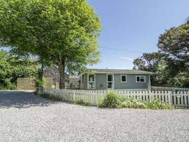 A single story house with a gravel driveway trees and a white picket fence at Orchard Lodge Llanengan near Abersoch