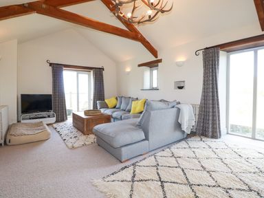 A living room with a gray sectional sofa with yellow pillows wooden coffee table and a television on a stand at Penpethy Farm in Tintagel