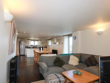 An open plan living room with a gray sectional sofa and wooden dining table with chairs at Penpethy Farm in Tintagel