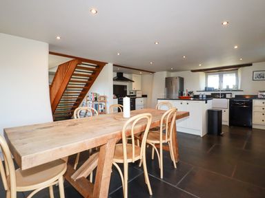 A kitchen and dining area with a wooden table and chairs next to a staircase at Penpethy Farm in Tintagel