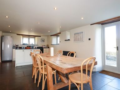 A kitchen and dining area with a wooden table and six chairs at Penpethy Farm in Tintagel