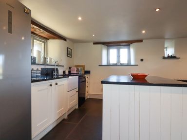 A kitchen with white cabinets a stainless steel refrigerator and a central island at Penpethy Farm in Tintagel