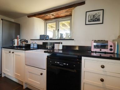 A kitchen with white cabinets black countertop a black dishwasher a pink toaster and a window with white pitchers at Penpethy Farm in Tintagel