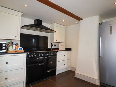 A kitchen with a black stove and hood white cabinets a silver refrigerator and countertop items at Penpethy Farm in Tintagel