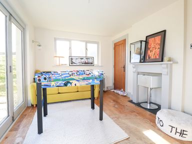 A game room with a foosball table yellow sofa and fireplace at Penpethy Farm in Tintagel