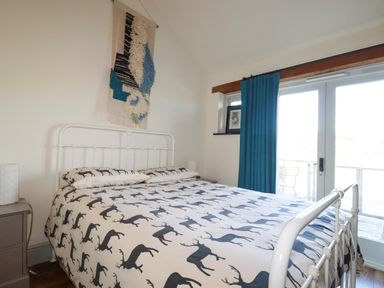 A bedroom with a bed with deer print bedding a wall hanging teal curtains and glass doors at Penpethy Farm in Tintagel