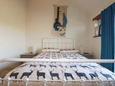 A bedroom with a white metal bed frame with deer print bedding and a wall hanging above at Penpethy Farm in Tintagel