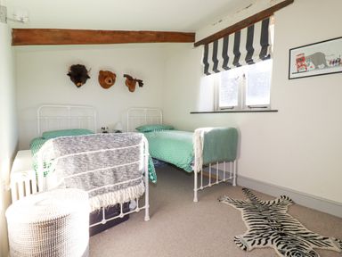 A bedroom with two single beds green checkered bedding animal head wall decor and zebra rug at Penpethy Farm in Tintagel