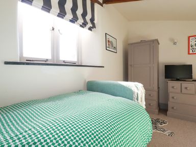 A bedroom with a bed covered by a green and white patterned blanket a wardrobe a chest of drawers a small television and a window with black and white striped curtains at Penpethy Farm in Tintagel