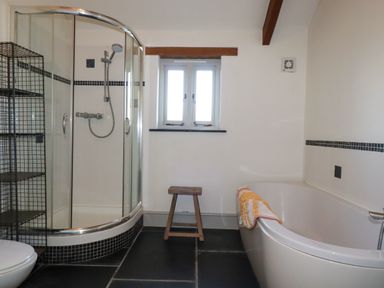 A bathroom with a shower enclosure a bathtub a wooden stool and a metal shelving unit at Penpethy Farm in Tintagel