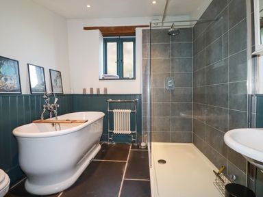 A bathroom with a freestanding bathtub framed pictures a window a shower with glass door and a sink at Penpethy Farm in Tintagel