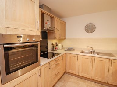A kitchen with wooden cabinets a built-in oven a stovetop a sink and a wall clock at Above & Beyond in Whitby