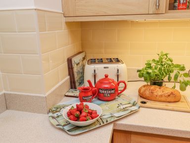 A kitchen counter with strawberries in a bowl a red teapot and creamer labeled Yorkshire Tea a toaster a loaf of bread on a cutting board and a potted plant at Above & Beyond Whitby