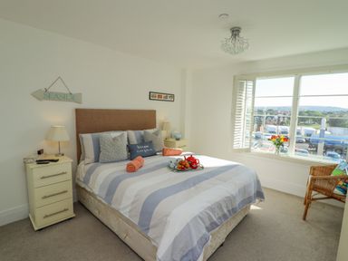 A bedroom with a bed striped bedding bedside tables lamps a chair and a window view at Above & Beyond in Whitby