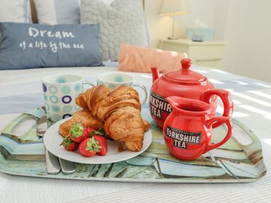 A breakfast tray with croissants strawberries red teapot and jug and two mugs on a bed at Above & Beyond in Whitby