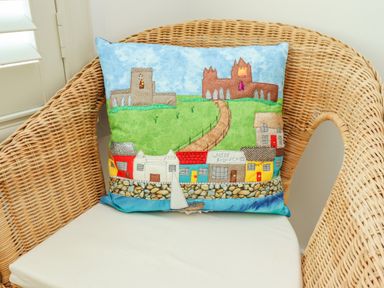 A wicker chair with a cushion featuring colorful houses and a path leading to buildings at Above & Beyond in Whitby