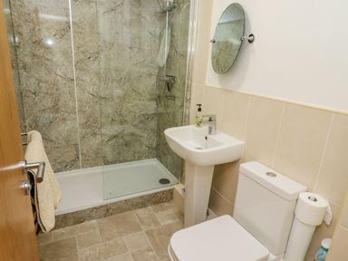 A bathroom with a shower area a sink a toilet a round mirror and a towel hanging on a door at Above & Beyond in Whitby