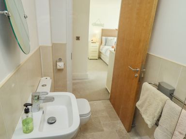 A bathroom with a sink toilet and towels on a rack with a view into a bedroom at Above & Beyond Whitby
