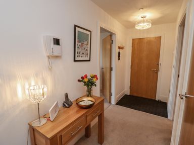 A hallway with a wooden console table holding a lamp flowers and a phone next to a wooden front door at Above & Beyond in Whitby