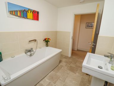 A bathroom with a bathtub flowers in a vase a sink and a door at Above & Beyond Whitby