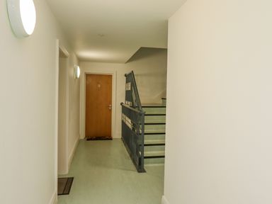 A hallway with a wooden door and a staircase with metal railing at Above & Beyond in Whitby