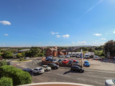 A parking lot with cars and trucks near a roundabout with flags and buildings in the background at Above & Beyond in Whitby