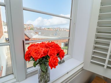 A bouquet of red roses in a glass vase on a windowsill with a view of rooftops and a cloudy sky at Above & Beyond in Whitby