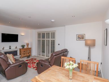 A living room with leather recliner chairs a wall-mounted TV and a wooden dining table with flowers at Above & Beyond Whitby