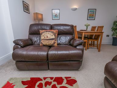 A brown leather sofa with a decorative pillow in front of a dining table with chairs and wall art at Above & Beyond Whitby