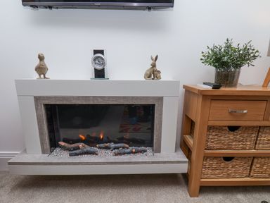A modern electric fireplace with decorative bird and rabbit sculptures on the mantel and a wooden side table with wicker baskets and a potted plant at Above & Beyond in Whitby