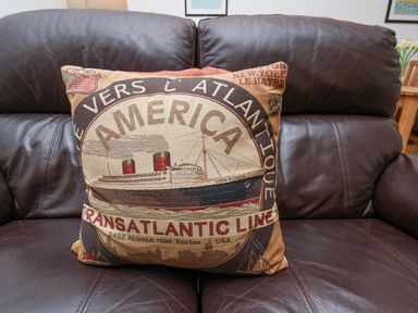 A pillow with a vintage ship design on a brown leather sofa at Above & Beyond in Whitby
