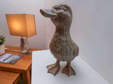 A wooden duck figurine on a white surface with a wooden table lamp and plant in the background at Above & Beyond in Whitby