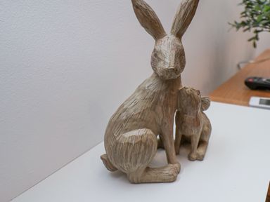A wooden sculpture of two rabbits on a white surface with a remote control on a wooden table in the background at Above & Beyond in Whitby