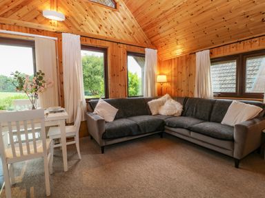 A corner living room with grey sofas and white dining table with chairs at Lodge 16 in Lanteglos near Camelford