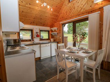 A kitchen and dining area with a white table set for four and a view of the outside at Lodge 16 in Lanteglos near Camelford