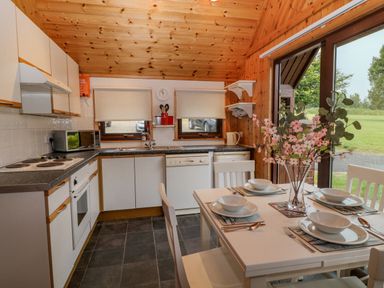 A kitchen with a dining table set with plates and bowls and a vase with flowers at Lodge 16 in Lanteglos near Camelford