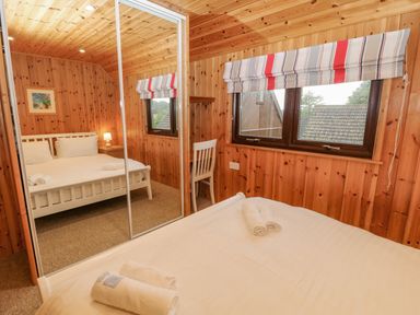 A bedroom with a double bed white furniture a chair and mirrored wardrobes at Lodge 16 in Lanteglos near Camelford
