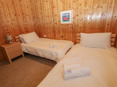 A bedroom with two single beds wooden walls and a small bedside table with a lamp at Lodge 16 in Lanteglos near Camelford