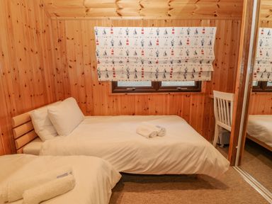 A bedroom with two single beds a window with patterned curtains a white chair and mirrored closet doors at Lodge 16 in Lanteglos near Camelford