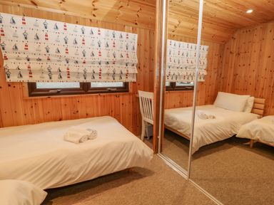 A bedroom with a wooden wall a bed with white bedding a chair and mirrored closet doors at Lodge 16 in Lanteglos near Camelford