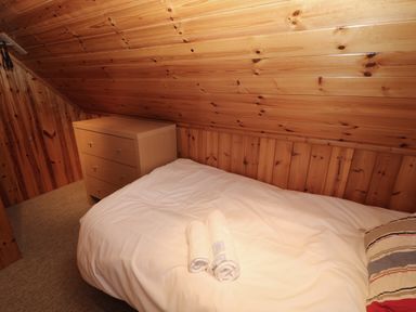 A small bedroom with a single bed and a wooden dresser under a sloped wooden ceiling at Lodge 16 in Lanteglos near Camelford