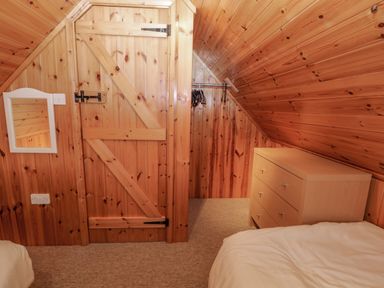 A bedroom with wood paneling a wooden door a small chest of drawers a bed and a mirror on the wall at Lodge 16 in Lanteglos near Camelford