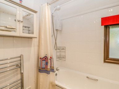 A bathroom with a bathtub a shower curtain a wall-mounted cabinet and a towel rack at Lodge 16 in Lanteglos near Camelford