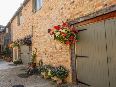 A brick building exterior with hanging flower baskets and large green doors at The Mews in Bovey Tracey near Chudleigh Knighton