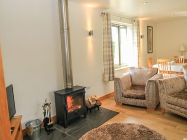 A living room with a wood burning stove armchairs and a dining table at The Mews in Bovey Tracey near Chudleigh Knighton