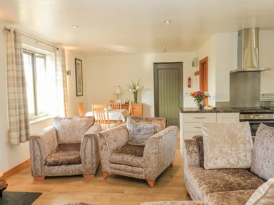 A living room with upholstered chairs and sofa near a dining table and kitchen area at The Mews in Bovey Tracey near Chudleigh Knighton