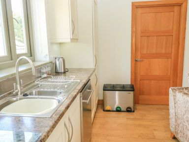 A kitchen with a double sink a kettle a dish rack and three waste bins on the floor near a wooden door at The Mews in Bovey Tracey near Chudleigh Knighton