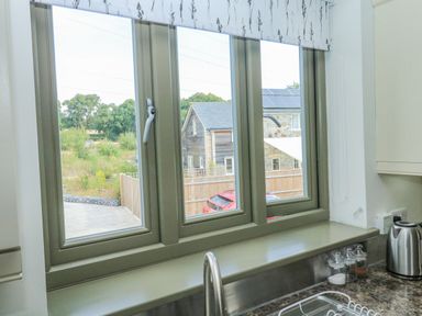 A kitchen window with a beige frame overlooking a garden and neighboring houses at The Mews in Bovey Tracey near Chudleigh Knighton